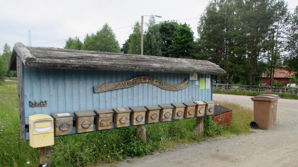 Rad med postlådor i trä och en gul brevlåda vid en landsväg i Sverige